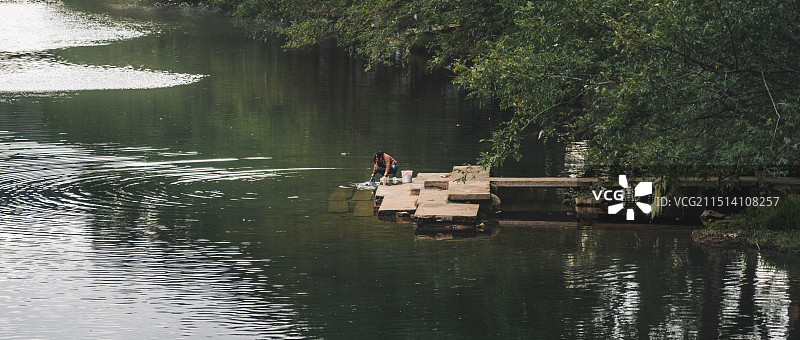 坐在湖边码头上洗衣服的老人的正视图图片素材