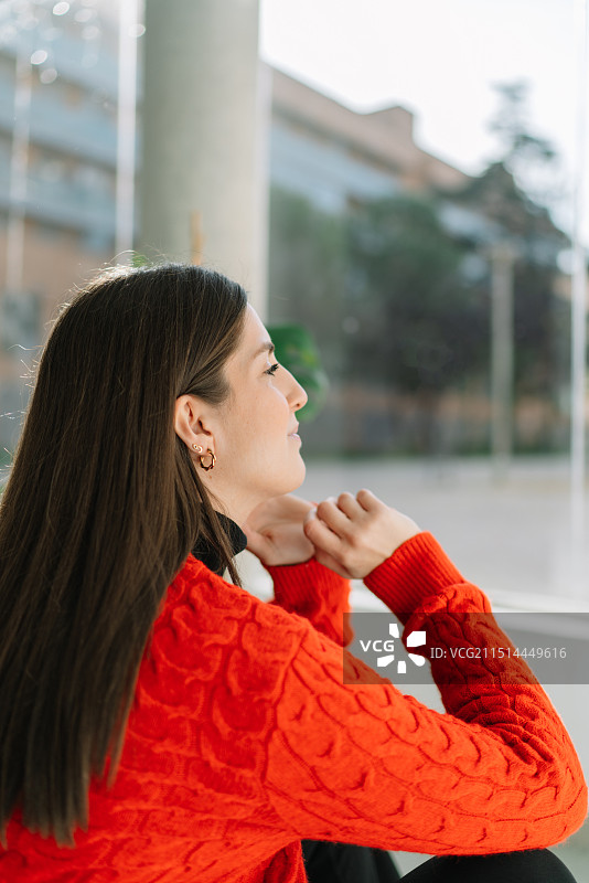 年轻女子坐在城市中，看向远方的侧视图图片素材
