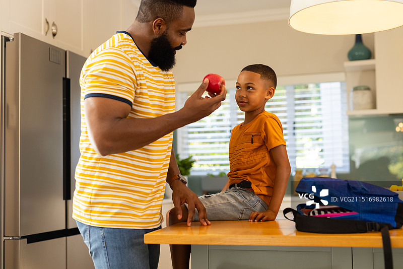 父亲拿着苹果，和坐在厨房柜台上的儿子说话，亲子时光图片素材