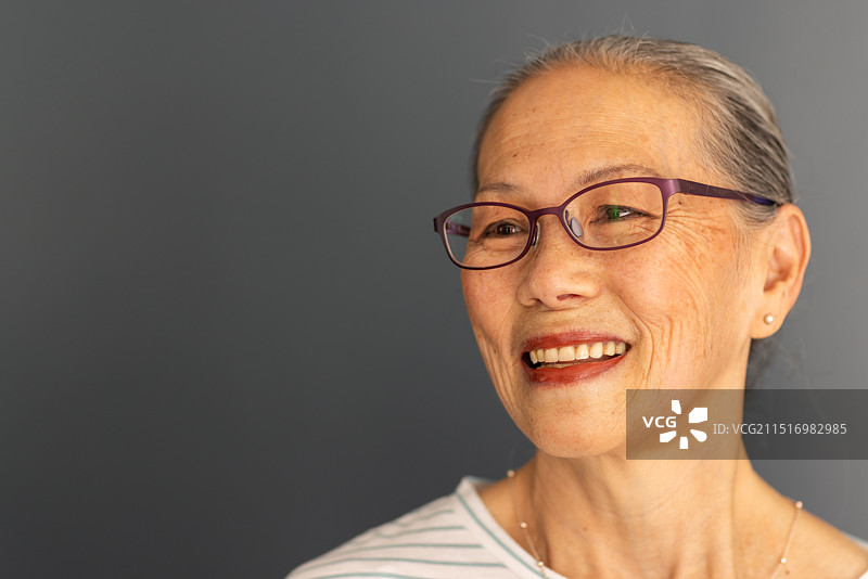 面带微笑的亚洲老妇人戴着眼镜望向远方，表现出幸福和满足图片素材