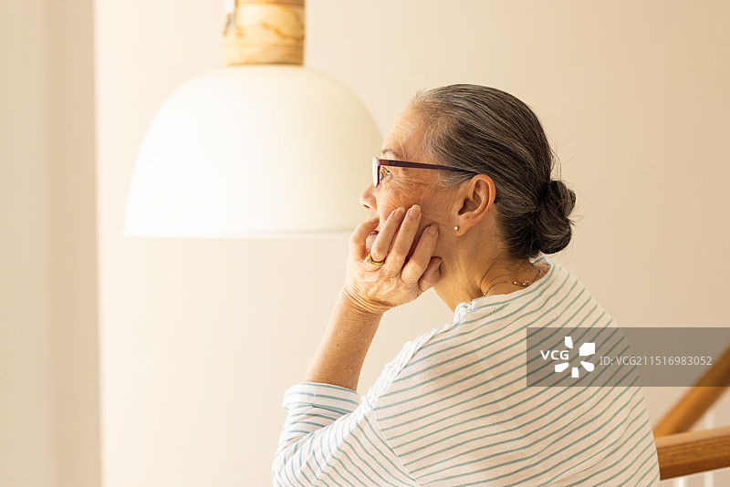 沉思的老年亚洲妇女戴着眼镜坐在灯下，若有所思图片素材