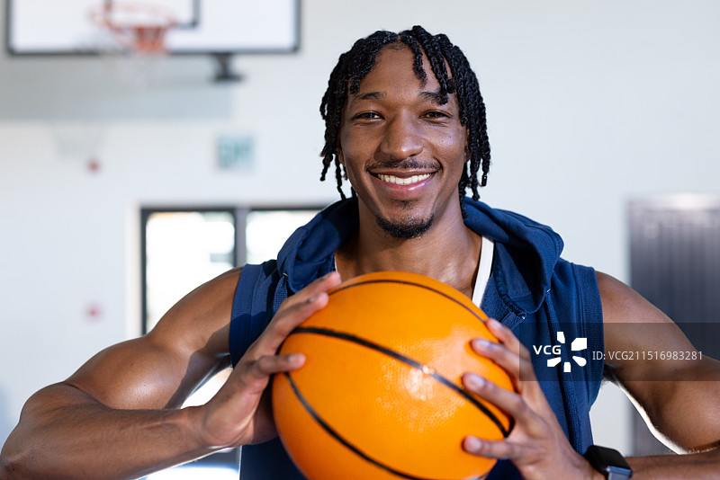 手持篮球在室内健身馆自信微笑的非洲裔男子图片素材