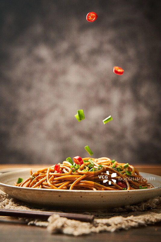 平拍热干面放在桌子上小辣椒葱花坠落图片素材