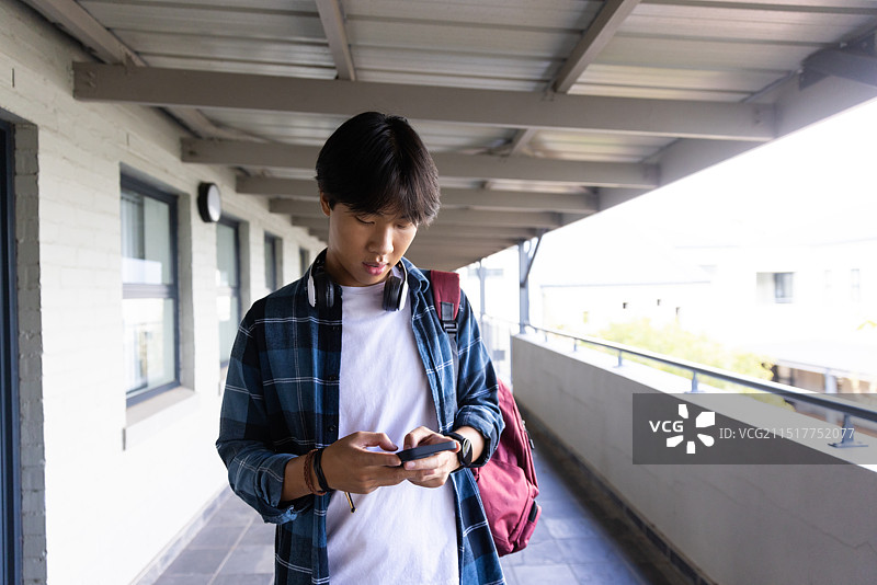 亚洲少年背着背包站在学校走廊里使用智能手机图片素材