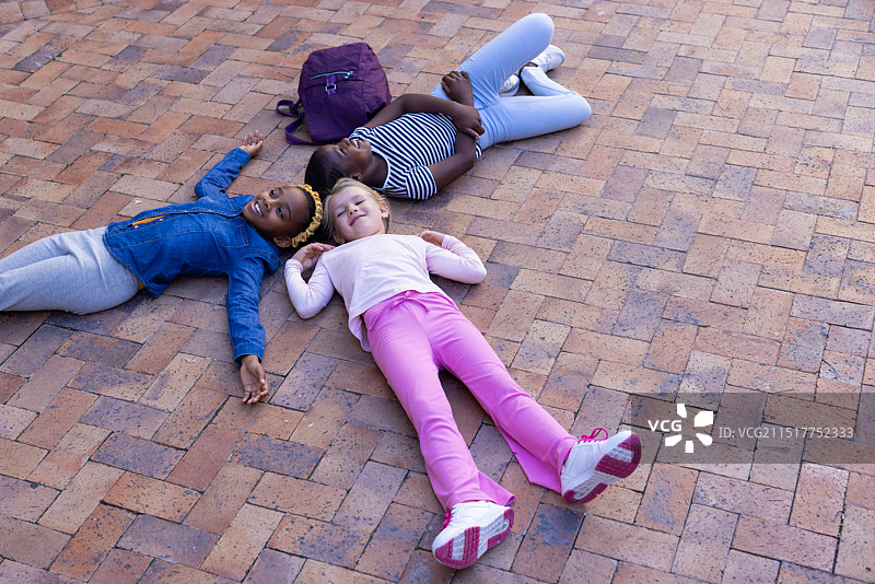 躺在砖砌路面上，三个不同种族女孩在学校附近背包放松图片素材