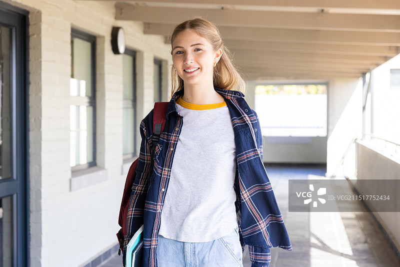 微笑的少女背着书包走在学校走廊里图片素材
