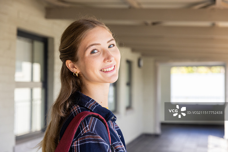 微笑的少女背着背包站在学校走廊里看着镜头图片素材