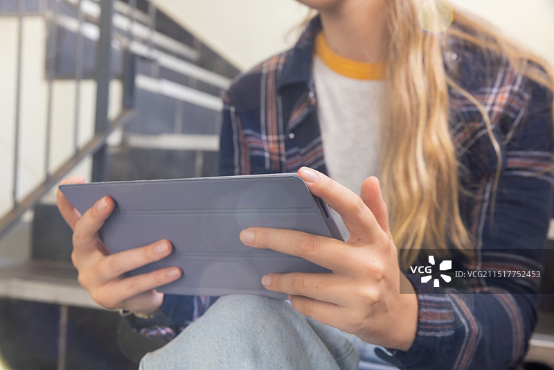 在学校环境中坐在楼梯上学习的青少年女孩使用平板电脑图片素材