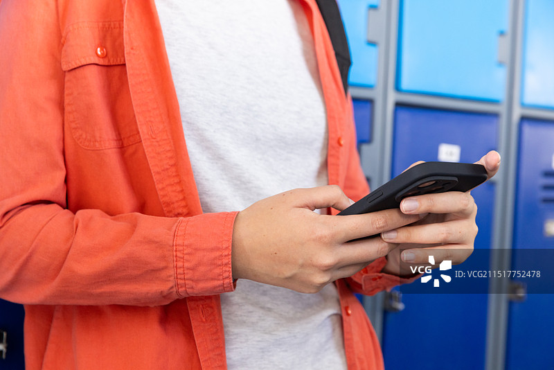 使用智能手机，少女穿着橙色外套站在学校的储物柜旁图片素材