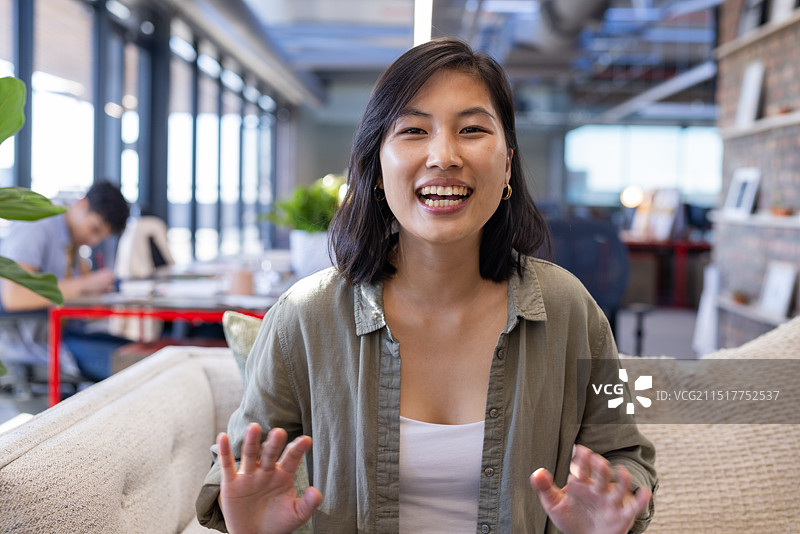 视频通话中，坐在现代办公室沙发上的微笑亚洲女人愉快地交谈图片素材