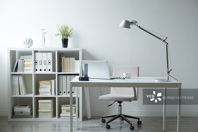 白色房间里，白色家具的桌子上放着文件、咖啡、眼镜和笔记本电脑图片素材