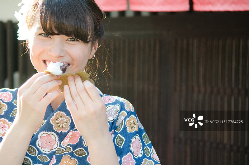 微笑的女人穿着和服，吃着用橡树叶包裹的年糕。图片素材