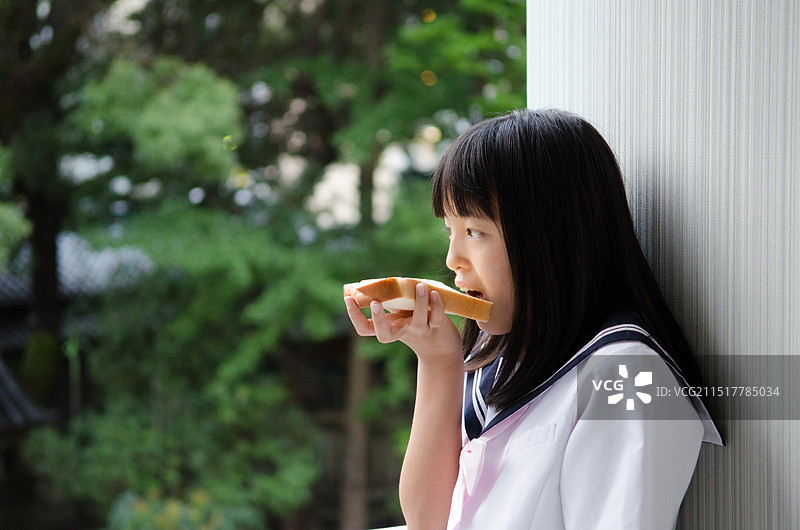 穿着制服靠墙吃面包的女孩图片素材