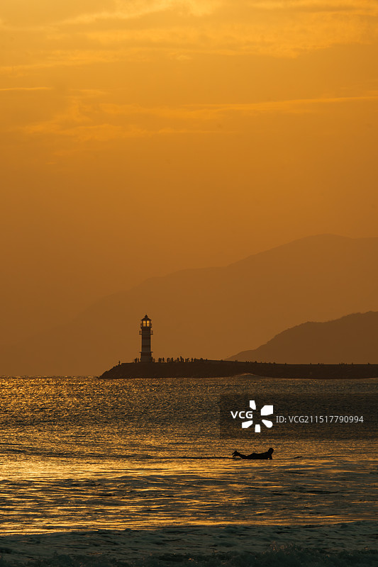 万宁神州半岛金色夕阳、海浪、远处灯塔和冲浪的人图片素材