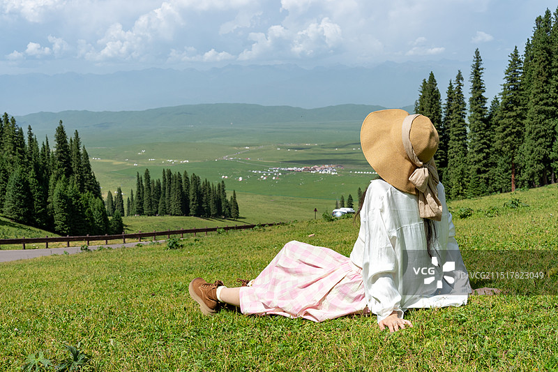 年轻女性坐在那拉提草原上眺望远方的背影图片素材