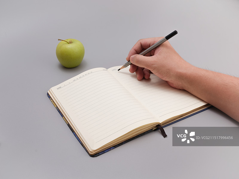 在灰白色背景上手握铅笔在笔记本上写字图片素材
