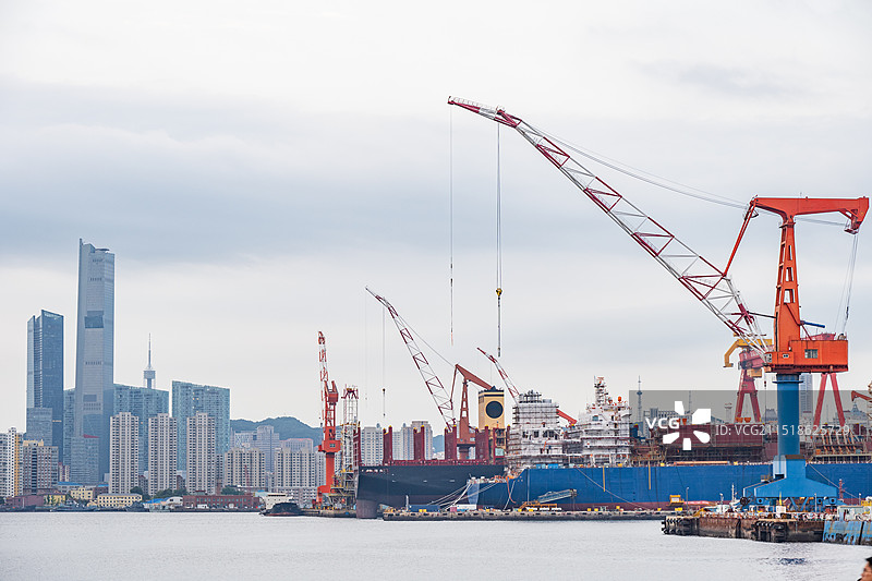 大连钻石湾造船厂的巨大吊车和远处的摩天大楼，繁忙的建设场景图片素材