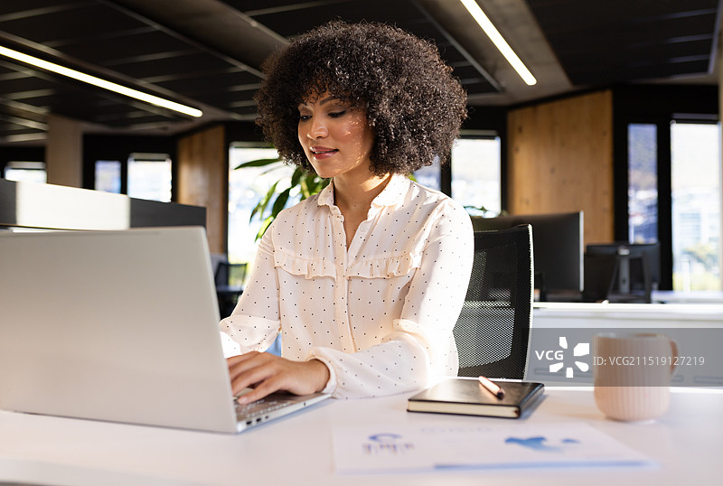 在办公室工作：使用笔记本电脑并专注做笔记的女性图片素材