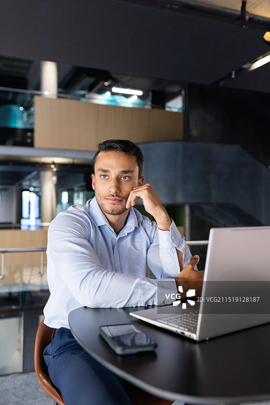 在现代办公室工作：男子使用笔记本电脑和智能手机，神情若有所思图片素材