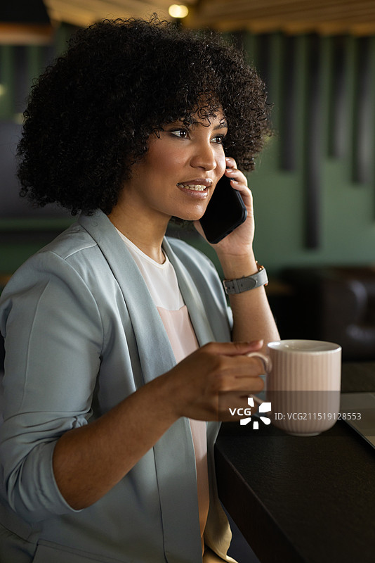 在办公室里，女人用智能手机交谈，拿着咖啡杯工作图片素材