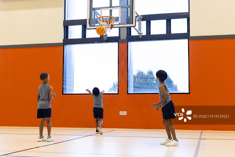 在学校体育馆打篮球，三个多种族男孩练习投篮，留白图片素材