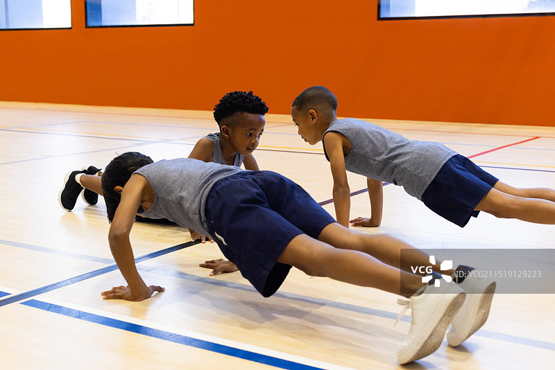 在学校体育馆里，三个多种族男孩在体育课上一起做俯卧撑图片素材