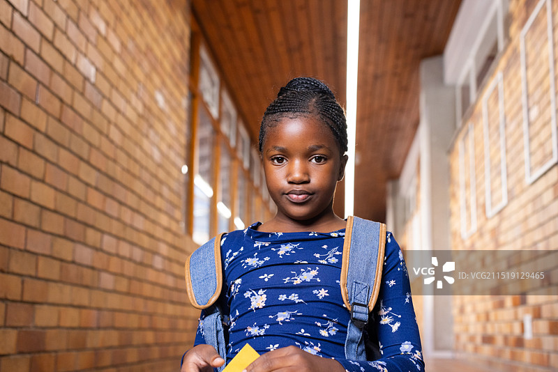 在学校，非裔美国女孩背着背包站在走廊里，看着镜头图片素材