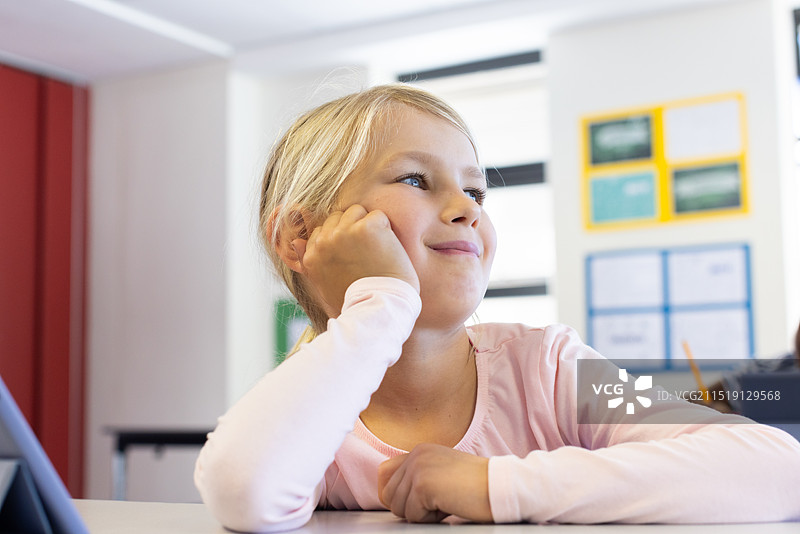 在学校里，女孩在课桌旁做白日梦，若有所思地望着远方图片素材