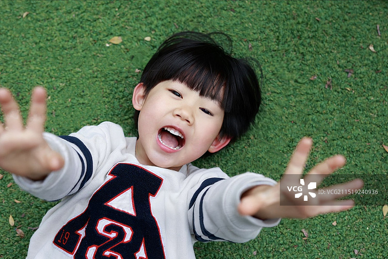 躺在草坪上张开嘴露出洁白牙齿的活力小男孩图片素材