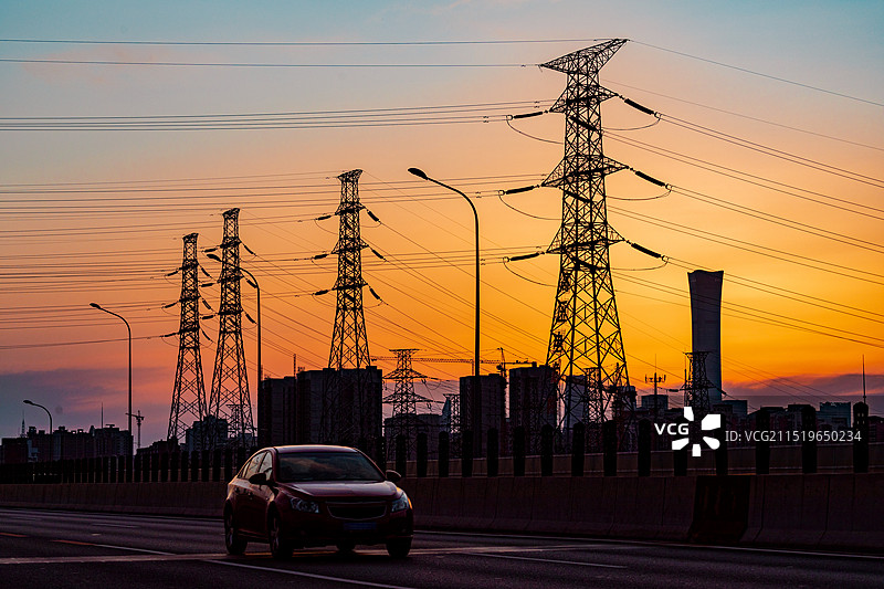 城市日落时分夕阳背景下的高压输电线路与道路上图片素材