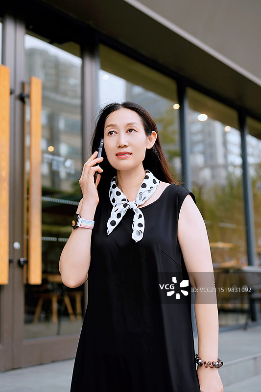 穿着黑色连衣裙、戴波尔卡圆点围巾的时尚女性在户外享受电话图片素材