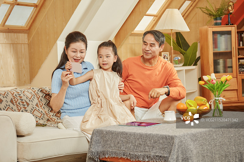 手拿手机与爷爷奶奶拍合影的小女孩图片素材