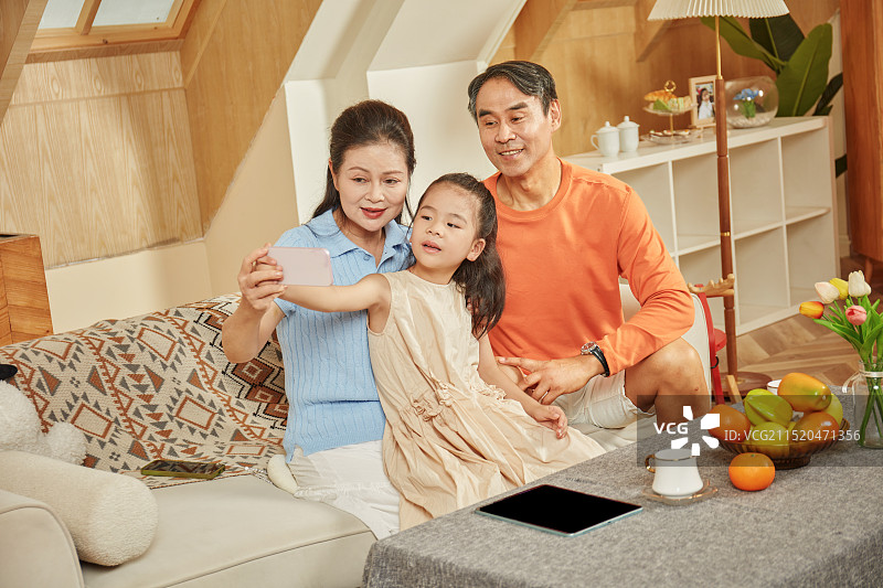 手拿手机与爷爷奶奶拍合影的小女孩图片素材