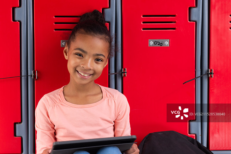 微笑女孩坐在红色学校储物柜前使用平板电脑图片素材