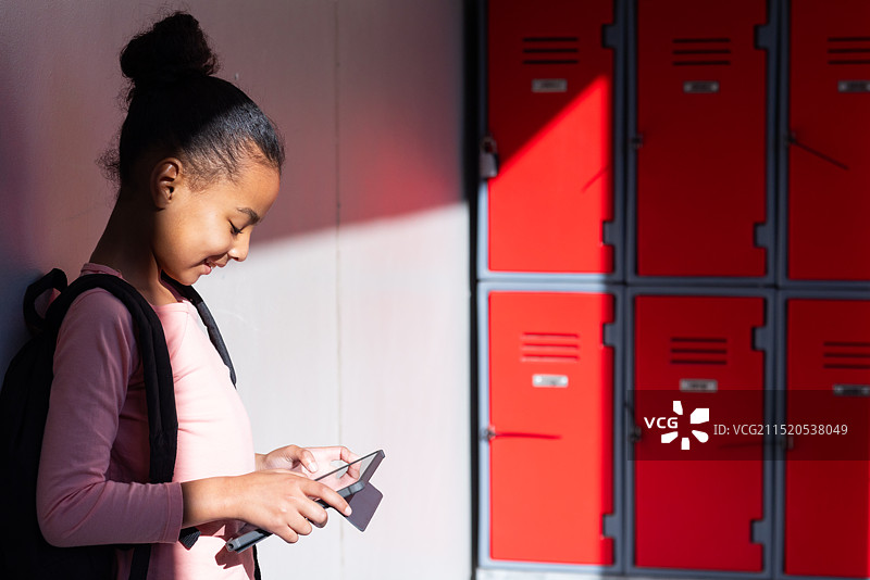 使用智能手机：女孩站在学校走廊的储物柜旁微笑图片素材