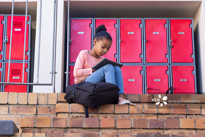 非洲裔女孩坐在学校储物柜前的台阶上看平板电脑图片素材