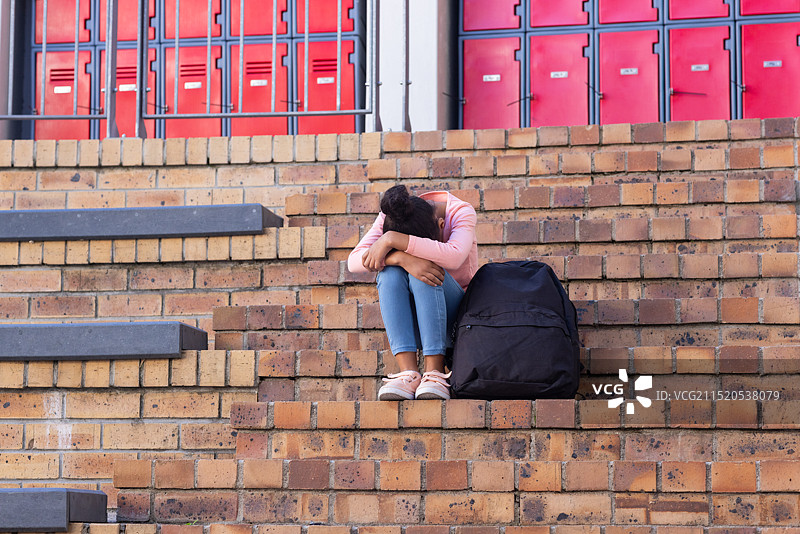 非裔美国女孩坐在学校台阶上，背着背包，感到悲伤和孤独图片素材