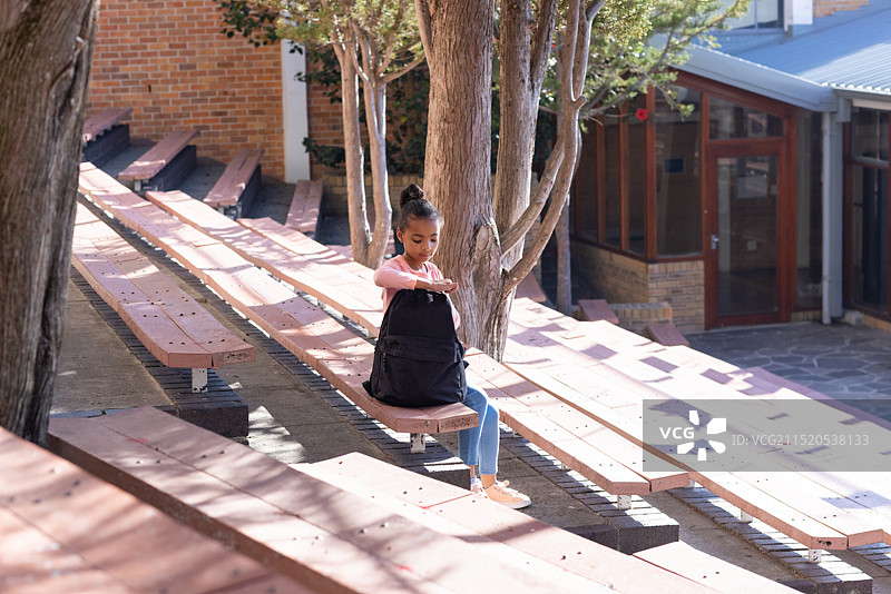 坐在长凳上，穿着校服的非裔美国女孩在户外查看背包图片素材