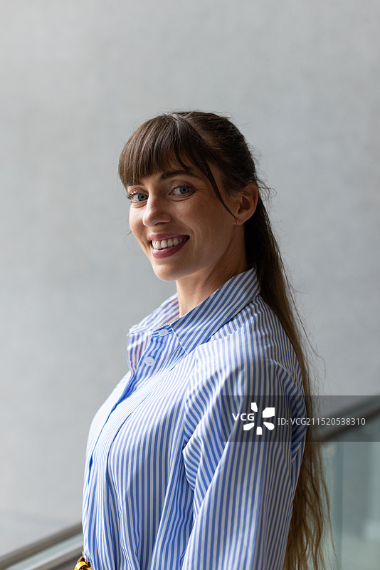 穿着条纹衬衫站在室内，看着镜头的微笑女人图片素材