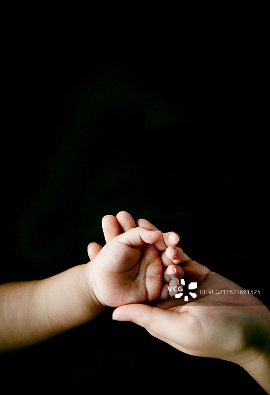 黑色背景上的婴儿和母亲的手图片素材