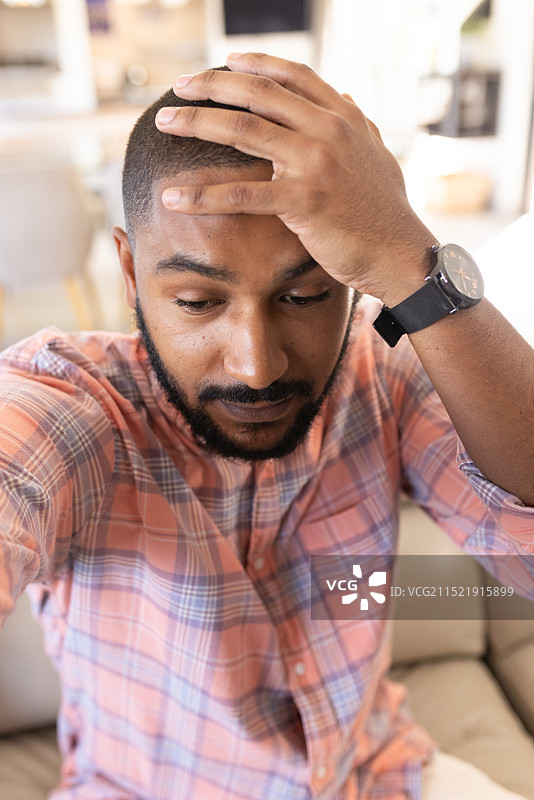印度男人坐在沙发上，穿着格子衬衫，手扶着头，压力很大，正在进行视频通话图片素材