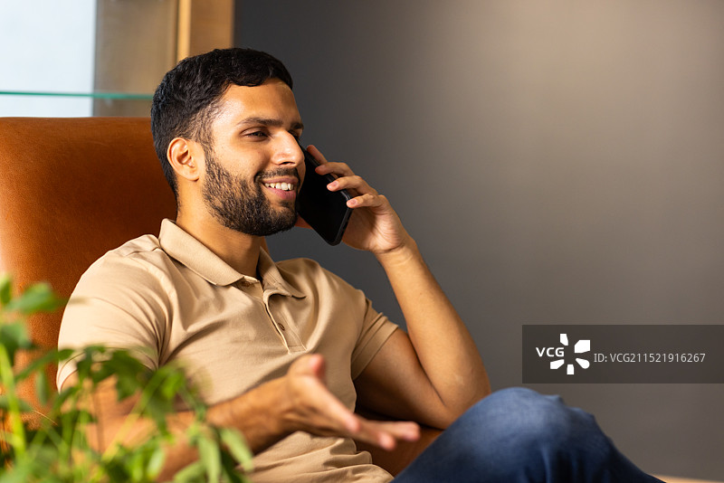 坐在椅子上用智能手机交谈，面带微笑，享受对话图片素材