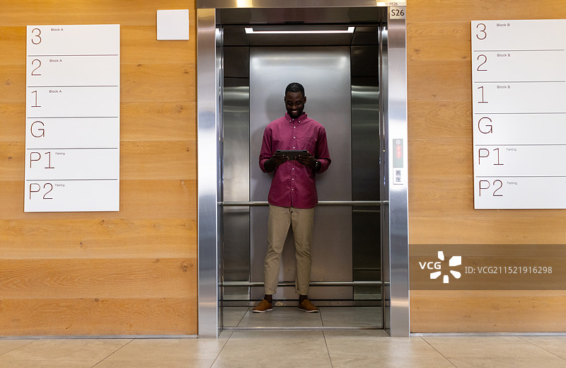 站在电梯里，男人使用平板电脑微笑，现代办公楼图片素材