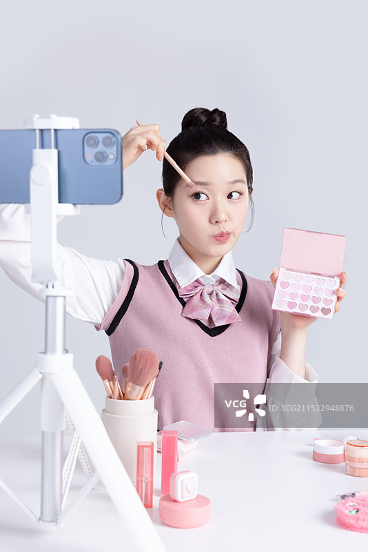 穿着校服的少女在展示化妆品并用手机拍摄视频图片素材