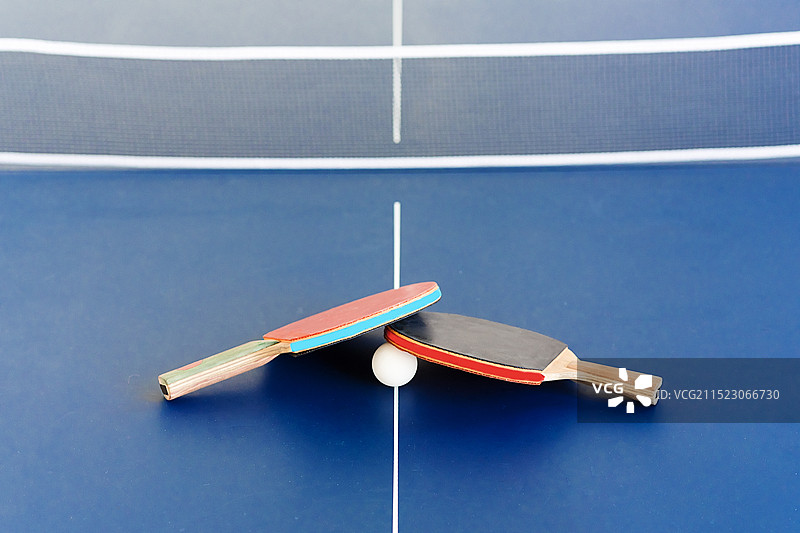 蓝色乒乓球桌上的红黑乒乓球拍和白色乒乓球网架图片素材