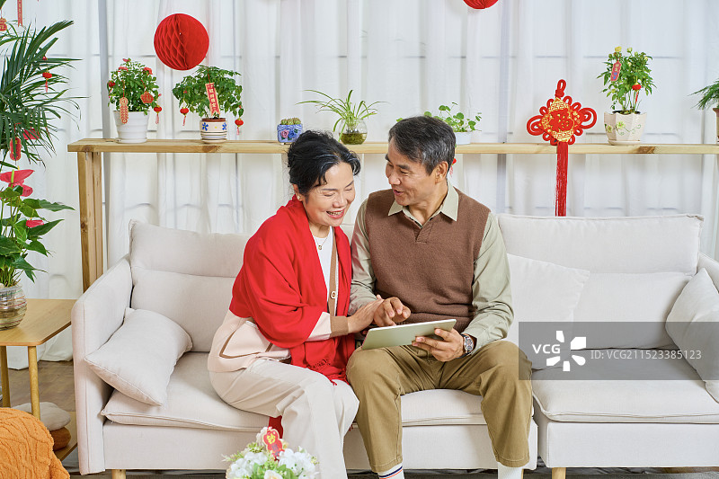 肩并肩坐在沙发上看平板电脑的老年夫妻图片素材