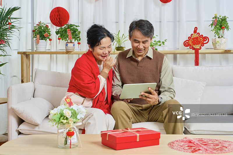 肩并肩坐在沙发上看平板电脑的老年夫妻图片素材