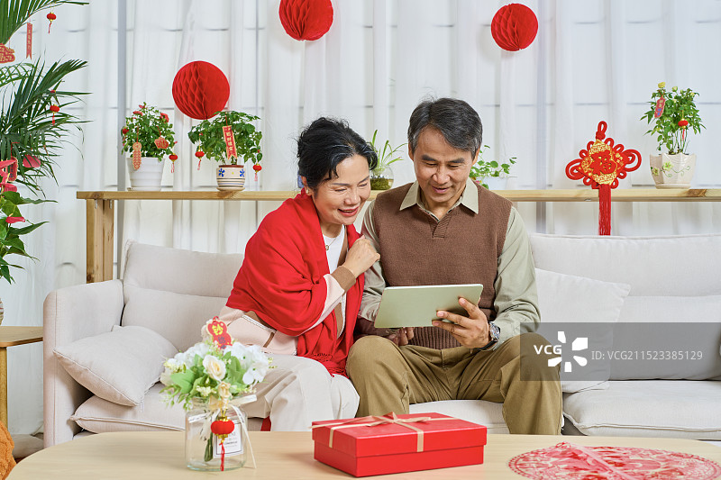 肩并肩坐在沙发上看平板电脑的老年夫妻图片素材