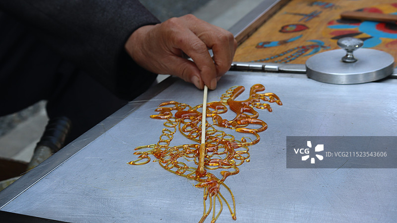 糖画匠人手持勺子作糖画龙的特写镜头图片素材