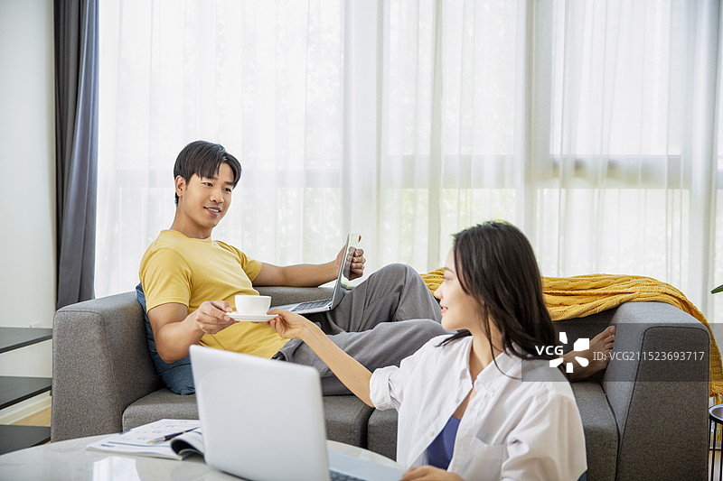 年轻情侣在客厅喝咖啡、使用笔记本电脑居家办公图片素材